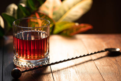 Faceted glass of whiskey with cocktail spoon on a wooden table 