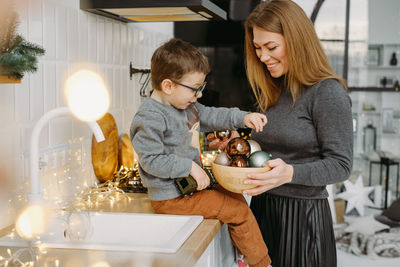 Mother and child on christmas kitchen paying with decor and baubles. woman with son prepare home for