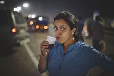 Close-up of young woman drinking beer at night