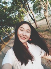 Portrait of smiling young woman against trees