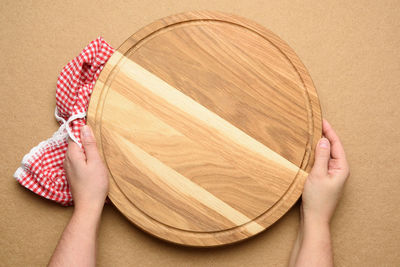 Woman holding empty round wooden pizza board in hand, body on a brown background, top view