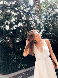 Woman with hand in hair standing against flowering plants