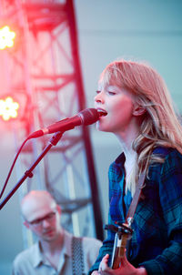 Young woman playing guitar while singing on microphone on stage