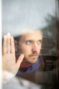 Portrait of young man looking through window