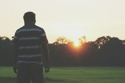 Rear view of man standing on field against sky during sunset