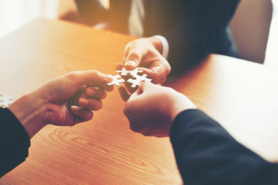 High angle view of people holding jigsaw piece on table