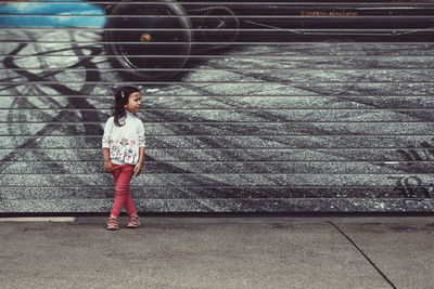 Girl standing on footpath against wall