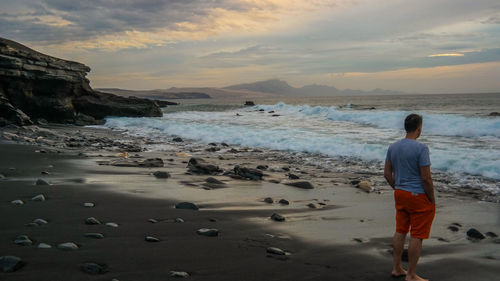 Rear view of man standing at beach against sky