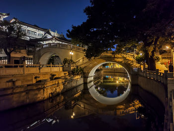 Illuminated bridge over river in city at night