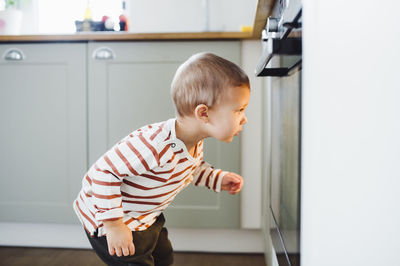 Toddler boy looking at oven in kitchen at home