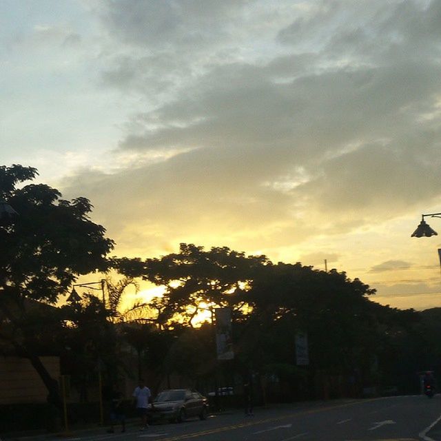 sunset, sky, transportation, car, tree, land vehicle, silhouette, mode of transport, cloud - sky, road, building exterior, street light, built structure, architecture, street, cloud, orange color, cloudy, outdoors, nature