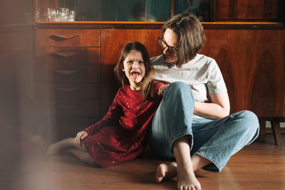 Emotional girl and her mother sitting on the floor in living room at home