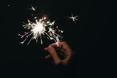 Cropped image of woman holding sparkler against black background