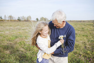 Happy grandfather with granddaughter holding chamomile flowers on field