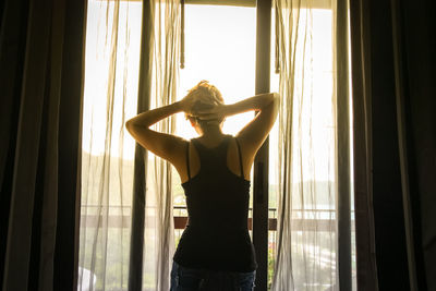 Rear view of woman standing by window at home