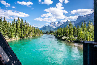 Scenic view from a bridge looking over a river with a forest and mountain setting and blue sky.