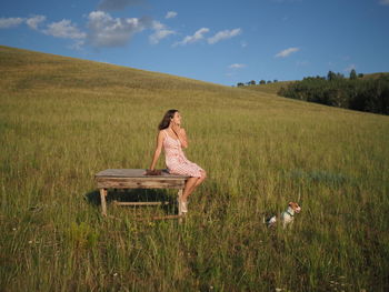 Rear view of woman sitting on field against sky