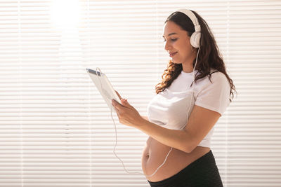 Side view of smiling young woman standing against wall