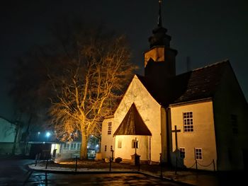 Illuminated street light by building against sky at night