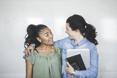 Smiling teenage high school student looking at teacher standing against whiteboard in computer lab