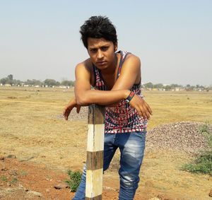 Portrait of young man standing on field against clear sky