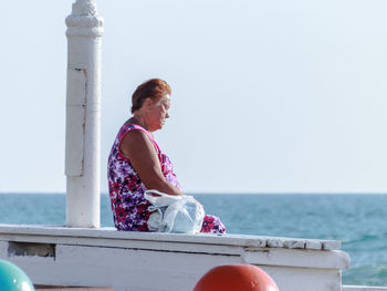 Woman sitting on pier by sea