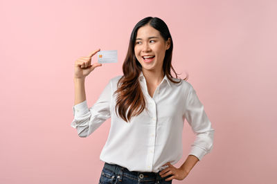 Portrait of young woman standing against pink background