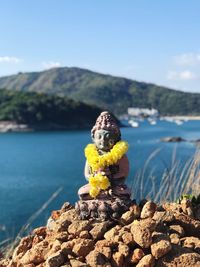 Floral garland on buddha statue by sea against mountains