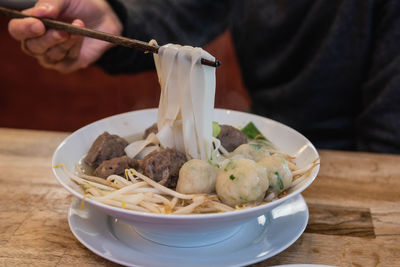 Man holding rice noodles with chopsticks, topping with meat balls and fish balls