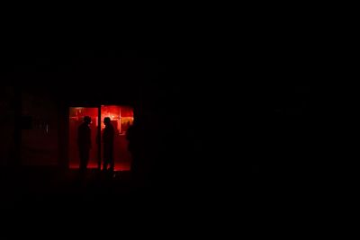 Silhouette people standing in illuminated dark room