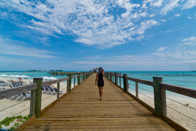 Rear view of woman walking on pier over sea against sky