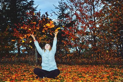 Full length of young woman throwing dry leaves in park during autumn