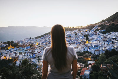 Rear view of woman standing by buildings against sky