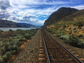 Railroad tracks leading towards mountains against sky