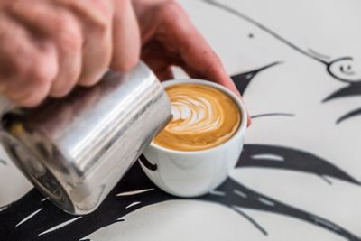 Cropped image of hand pouring milk in coffee cup on table