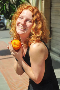 Portrait of smiling woman holding orange fruit in city