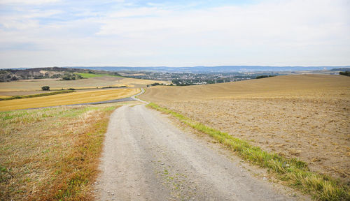 Dirt road in the middle of a mown wheat field, large areas of stubble visible.