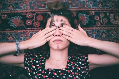 High angle view of woman covering eyes with hands while lying on carpet