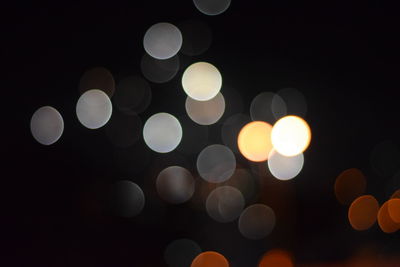 Defocused image of illuminated lights against sky at night