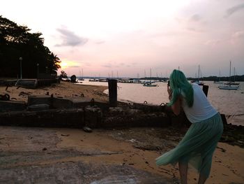 Rear view of woman on beach against sky during sunset