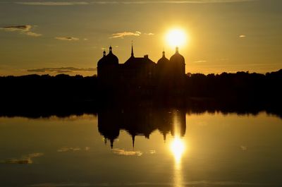 Silhouette temple by lake against sky during sunset