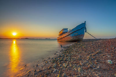 Boat moored on beach against sky during sunset