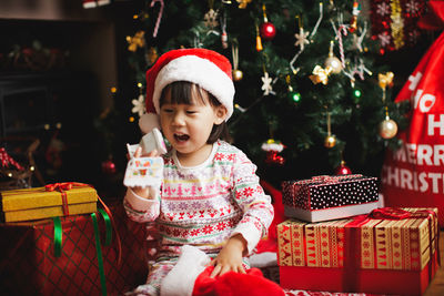 Cute girl holding toy while sitting by christmas presents at home