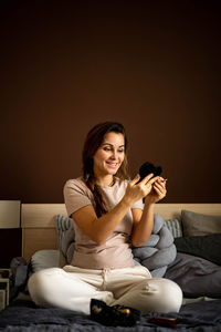 Portrait of woman applying makeup while sitting on bed