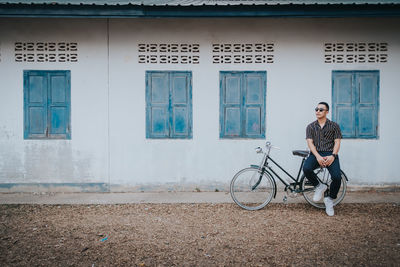 Full length of man sitting outside house on bicycle