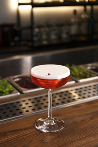 A glass of red alcohol drink with foam and flower petal. cocktail garnish. vertical orientation.