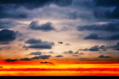 Low angle view of silhouette airplane flying against dramatic sky