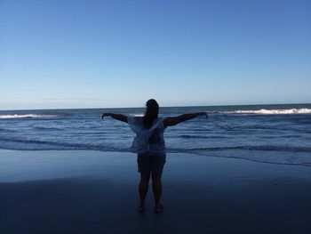 Rear view of woman standing on beach against clear sky