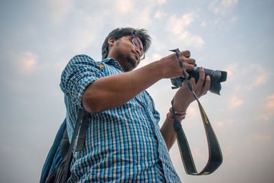 Low angle view of man photographing against sky