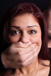 Man covering woman mouth with hand against black background